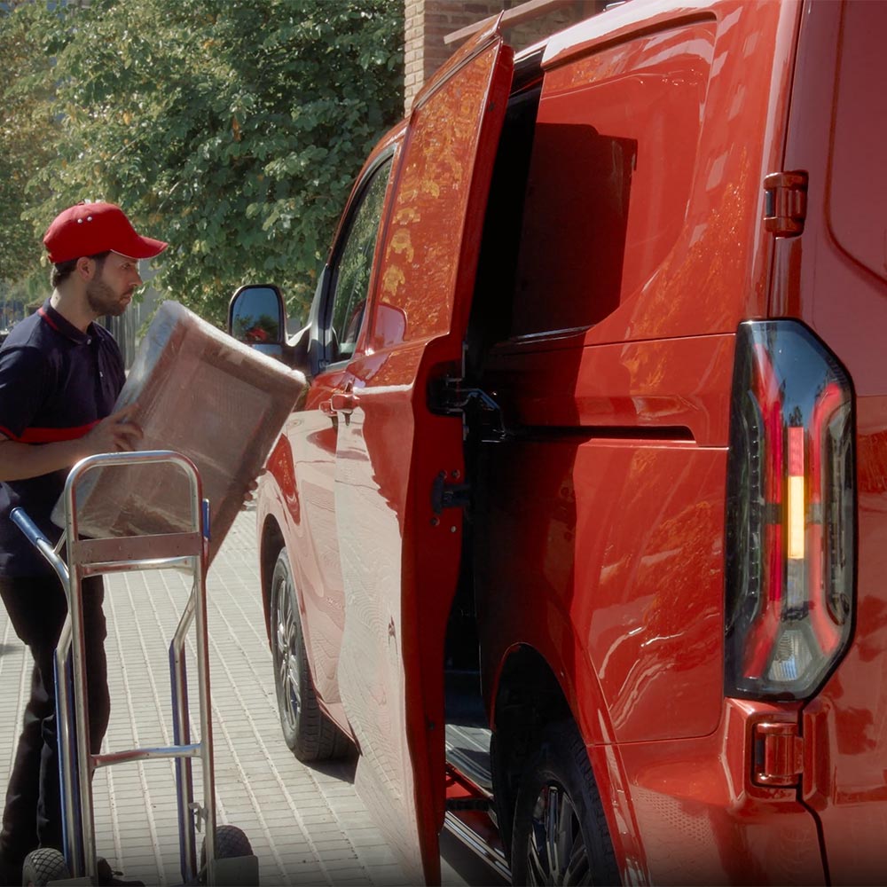 Un livreur décharge des colis d’un Ford Transit Custom rouge.