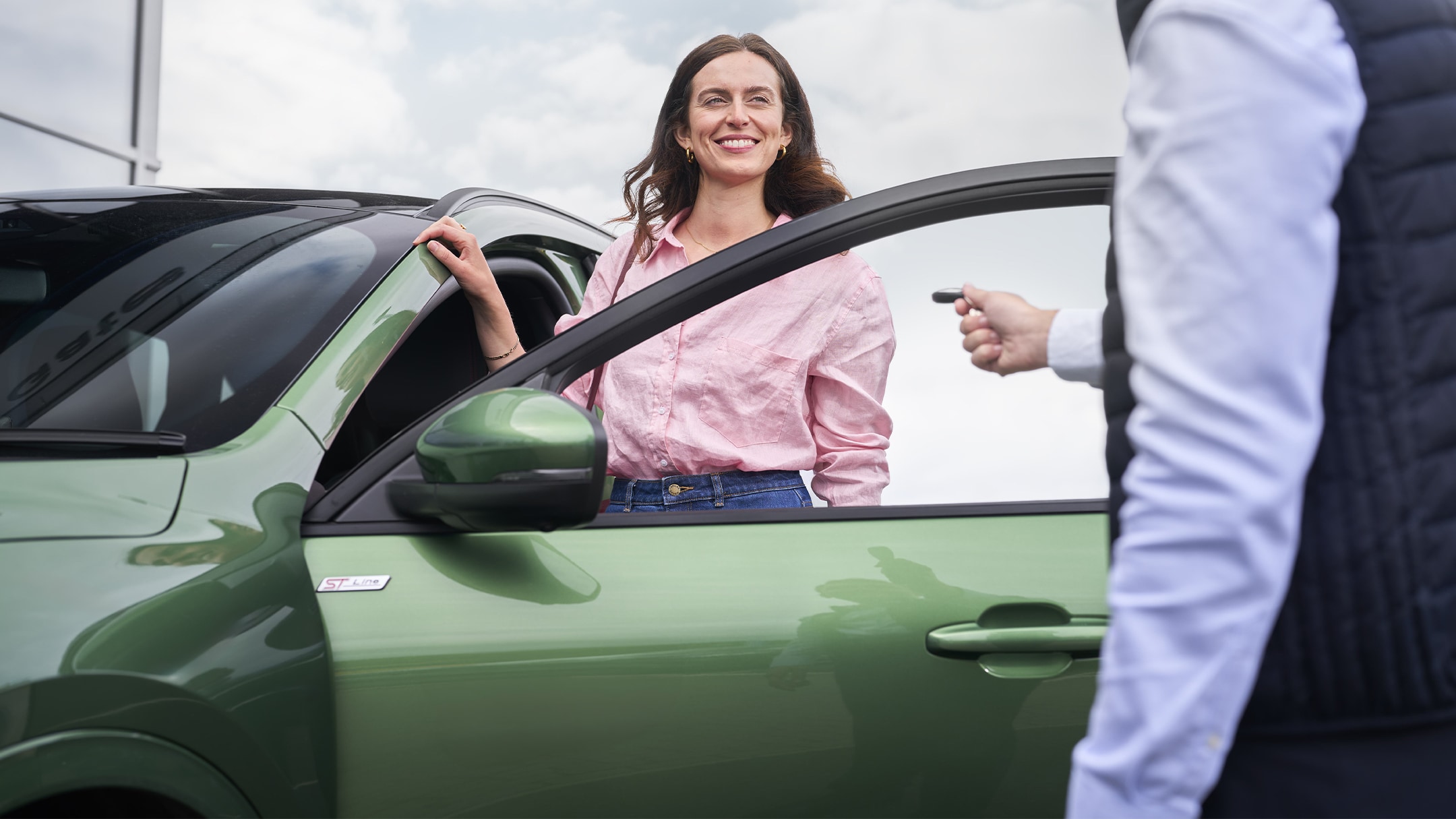 Une femme vêtue d’une chemise rose souriant à côté d’une voiture verte, avec un conseiller Ford qui lui remet ses clés de voiture. 