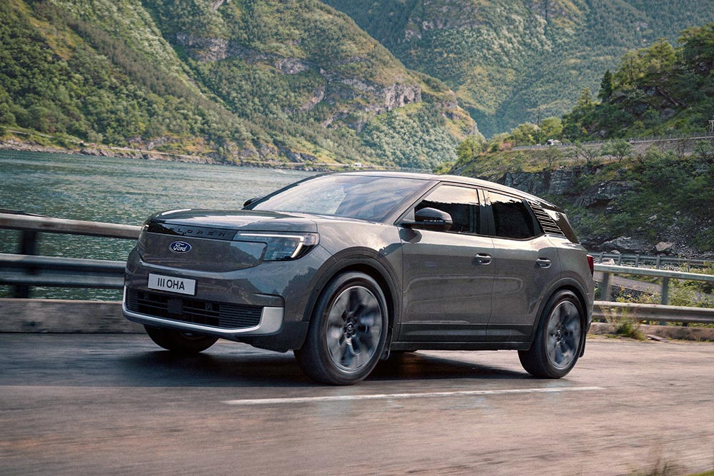 Un Ford Explorer gris roulant sur une route de montagne le long d'un fjord, avec en toile de fond des montagnes boisées.