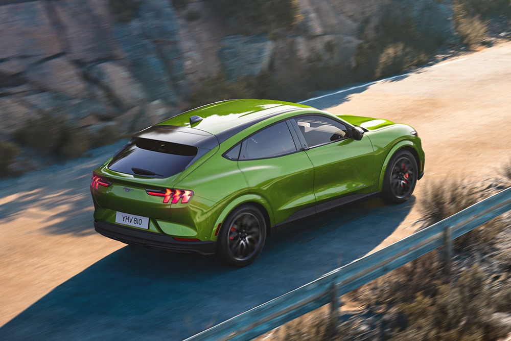 Une Ford Mustang Mach-E verte filant à toute allure sur une route de montagne sinueuse.