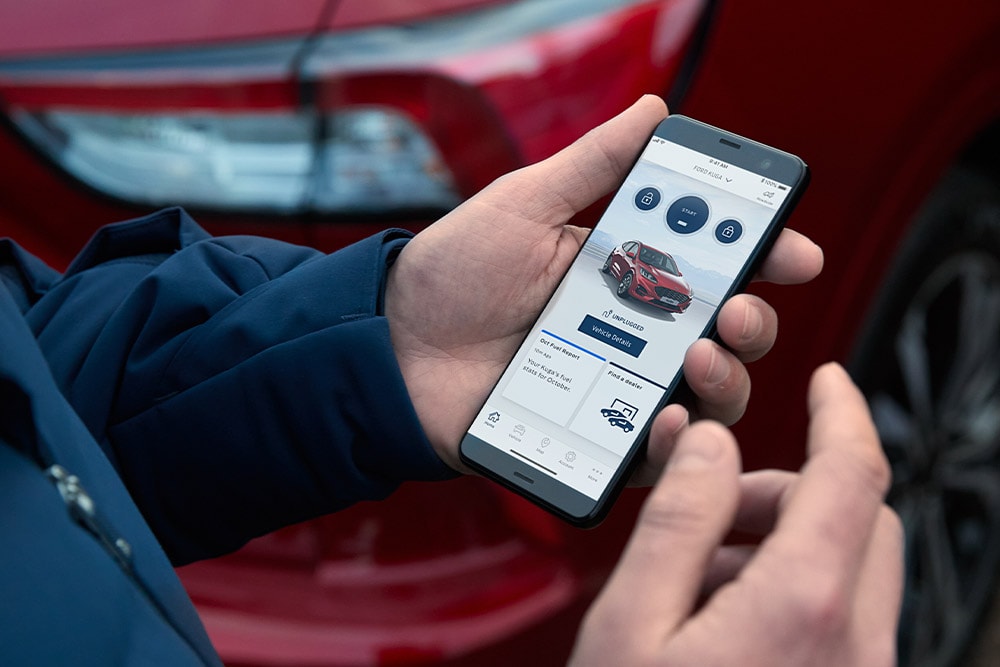 Personne tenant un smartphone affichant l'application FordApp avec un Ford Kuga rouge.