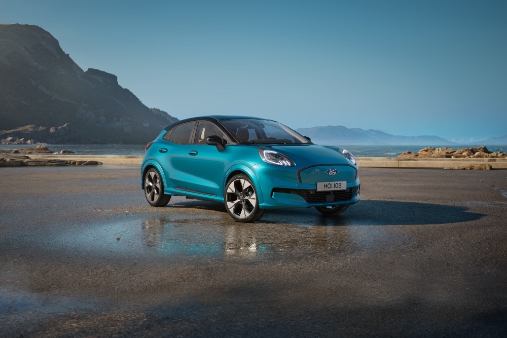 Un Ford Puma Gen-E bleu sur une plage mouillée sous un ciel bleu.