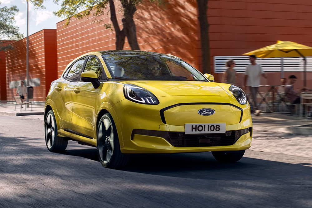 Ford Puma Gen-E jaune passant devant la terrasse d'un café