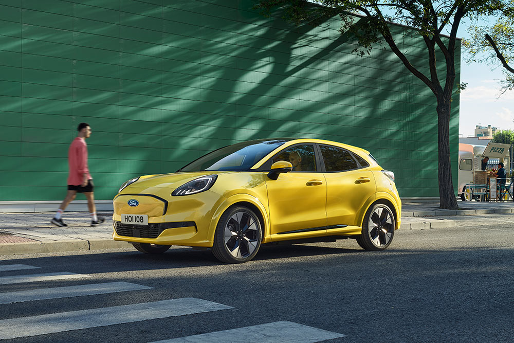 Un Ford Puma Gen-E jaune vif garé sur un passage piéton dans une rue urbaine ensoleillée.
