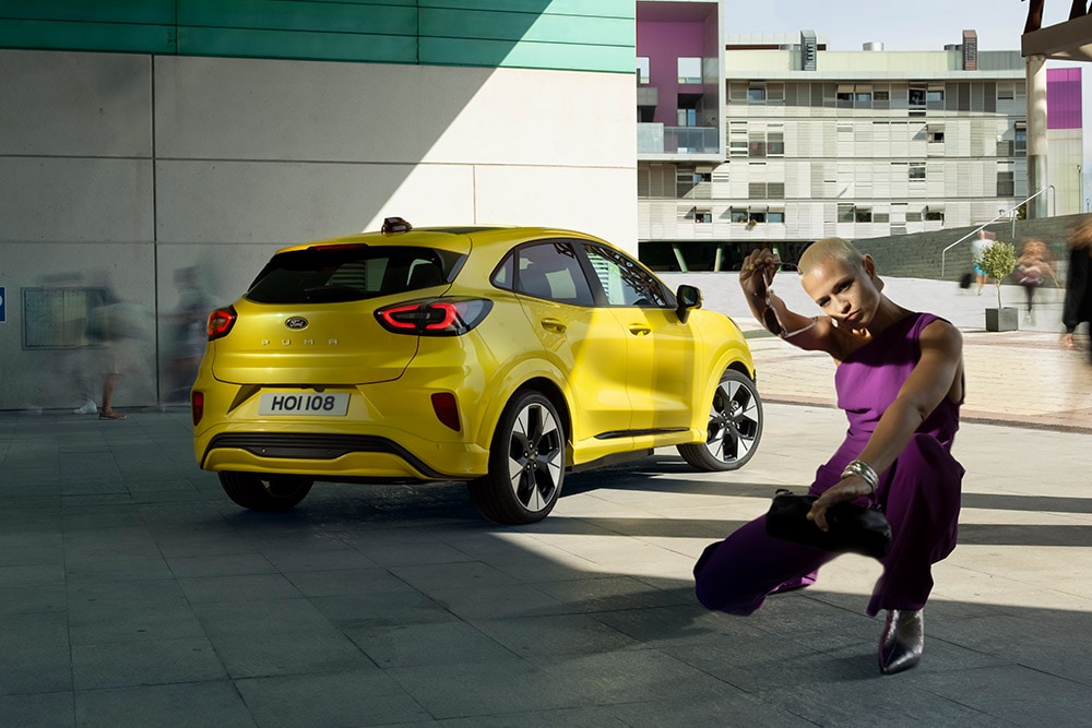Un Ford Puma Gen-E jaune vif est garé dans un environnement urbain, vue de l'arrière.
