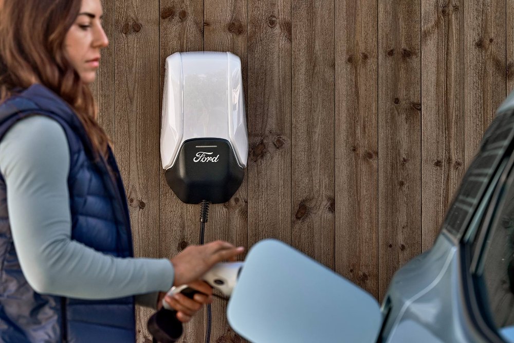 Une femme branche son véhicule électrique Ford Explorer bleu sur une borne de recharge domestique.