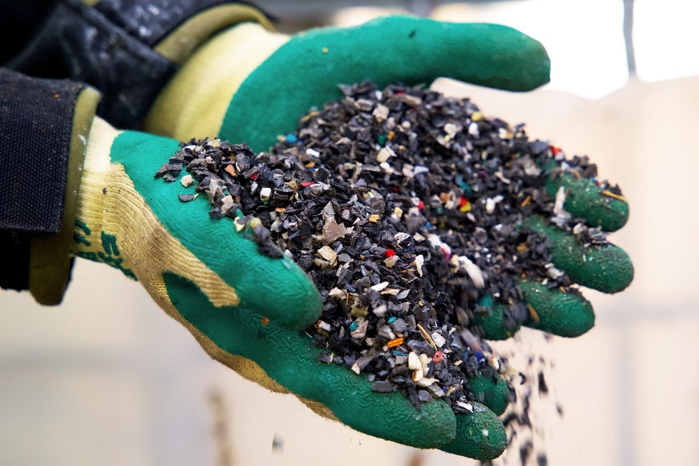 Mains gantées de caoutchouc tenant des morceaux de déchets plastiques recyclés.