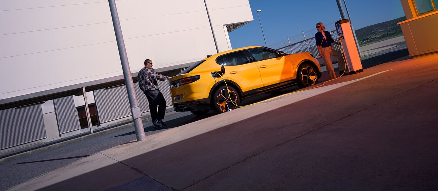 Des personnes rechargent un Ford Capri EV jaune à une station de recharge publique.