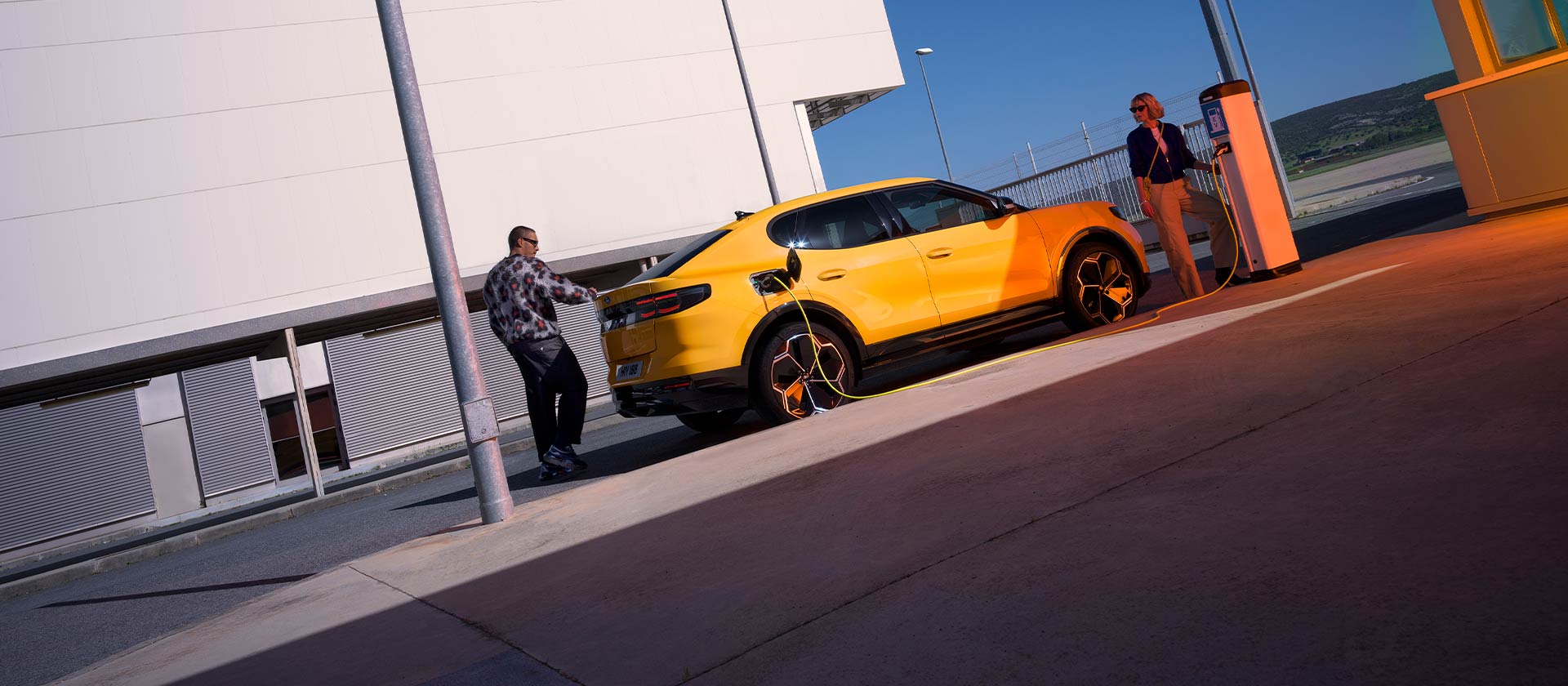 Des personnes rechargent une Ford Capri EV jaune à une station de recharge publique.
