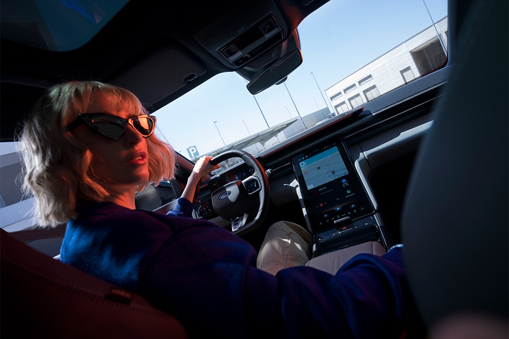 Une femme est assise au siège conducteur du Ford Capri électrique, montrant également le grand écran tactile SYNC Move de 14,6 pouces.