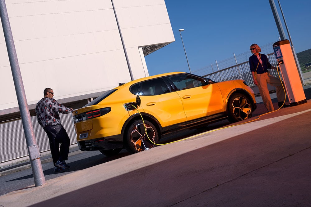 Des personnes rechargent un Ford Capri EV jaune à une station de recharge publique.
