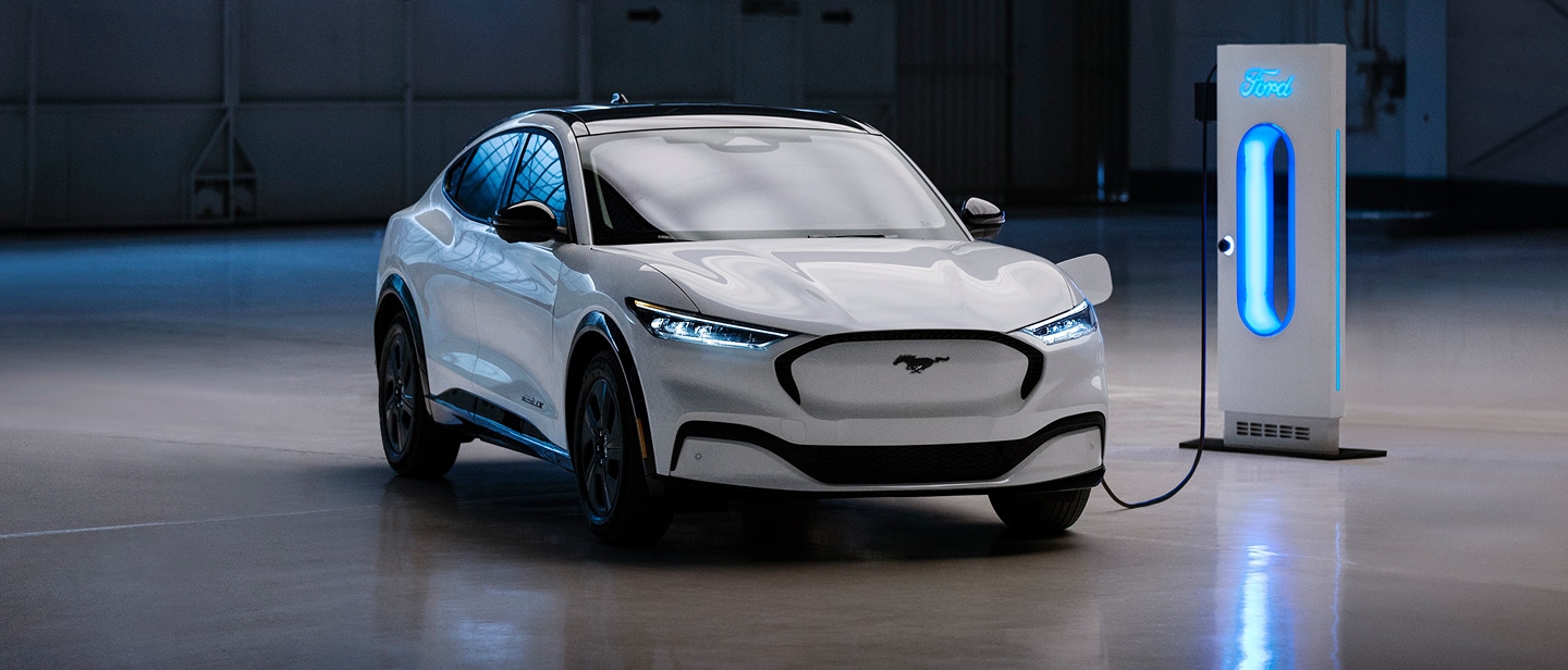 Une Ford Mustang Mach-E blanche garée dans un garage, branchée à une station de recharge bleue brillante.