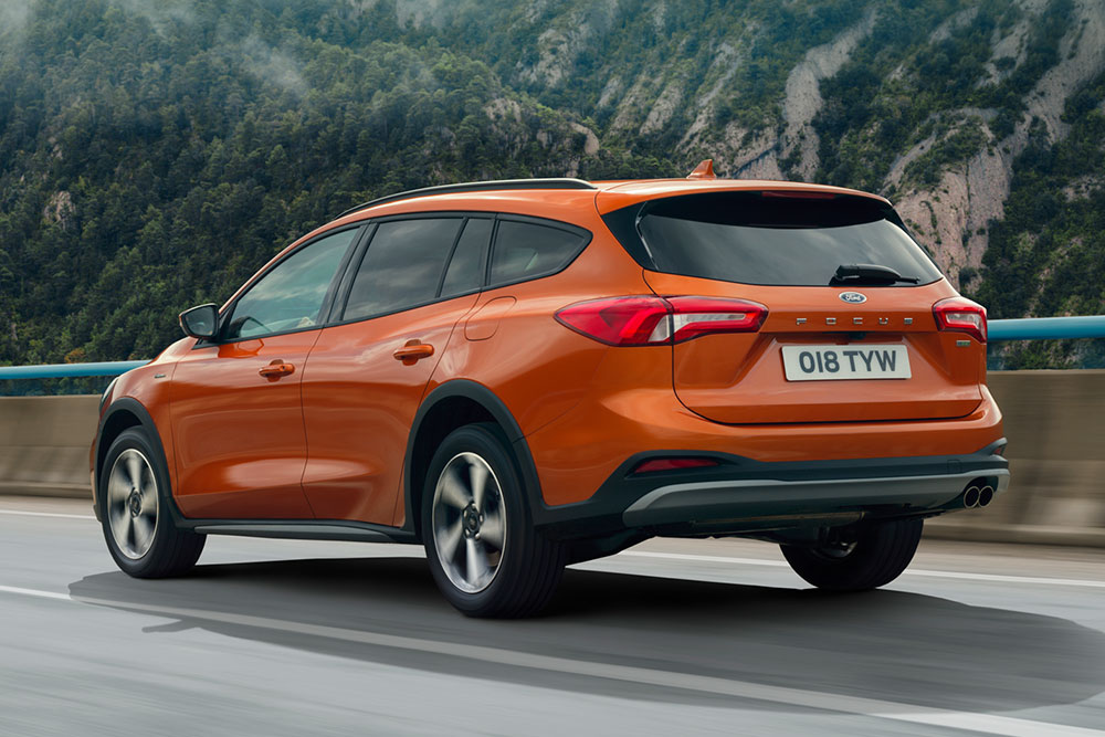 Vue arrière 3/4 d'un Ford Focus orange sur une route de montagne brumeuse.