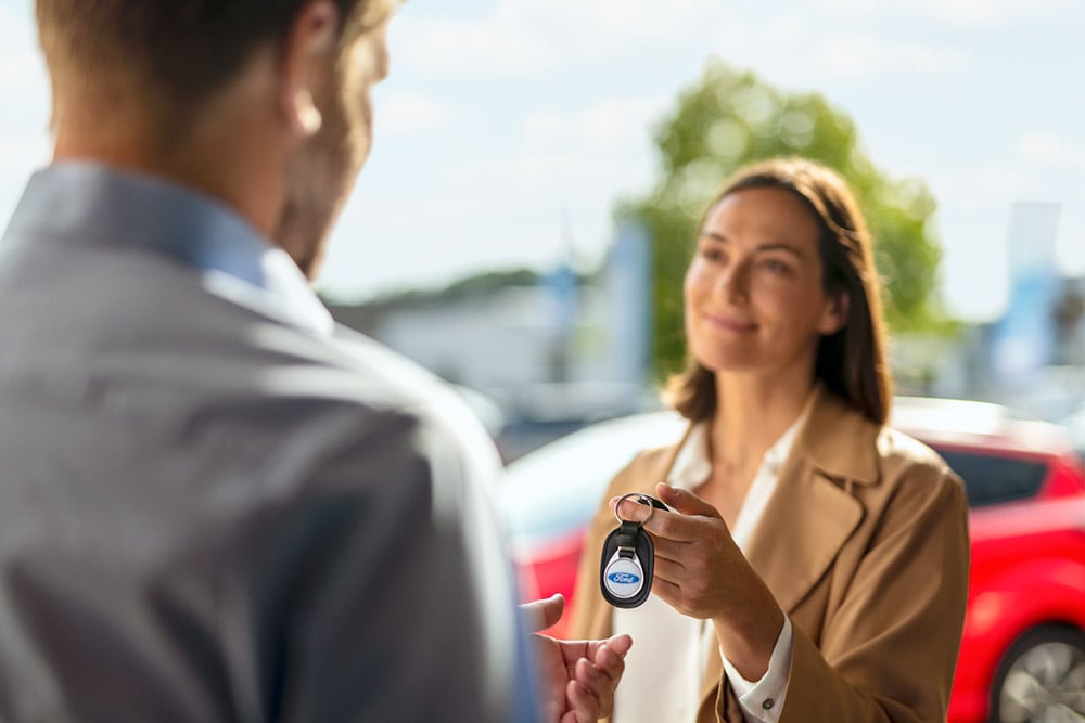 Une femme remet les clés d'une voiture Ford à un homme.