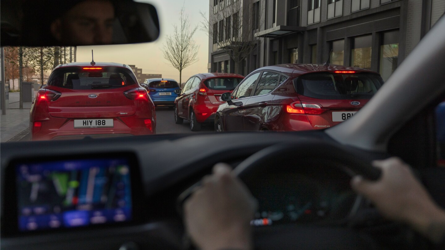 Cockpit view of a Ford, with the traffic ahead seen through the windshield.