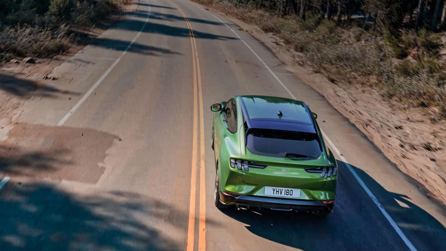 Ford Mustang Mach-E GT Eruption Green roulant sur une route de montagne bordée d’arbres.