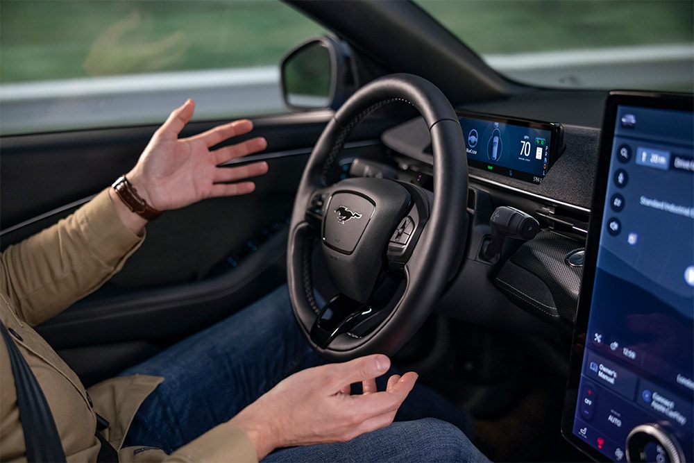 Homme au volant de la Mustang Mach-E, expliquant avec ses mains la technologie de conduite autonome BlueCruise