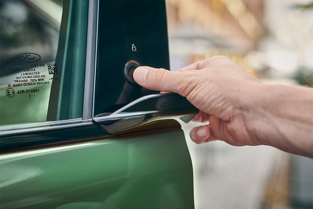 Gros plan d’une main actionnant le système E-Latch en appuyant sur un bouton de la porte d’une Ford Mustang Mach-E verte.