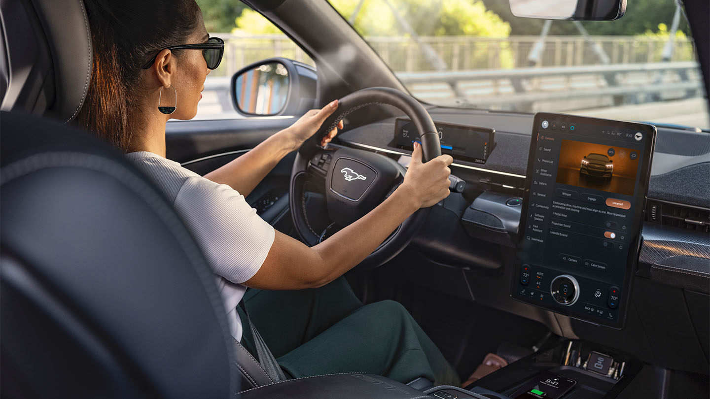 Une femme conduisant la Mustang Mach-E avec ses mains sur le volant. L’écran tactile de 15,5" indiquant des informations sur la voiture.