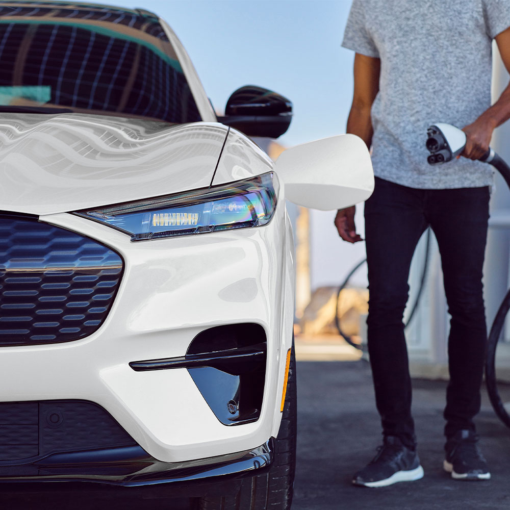 Personne chargeant une Ford Mustang Mach-E blanche avec un câble de recharge pour véhicule électrique.