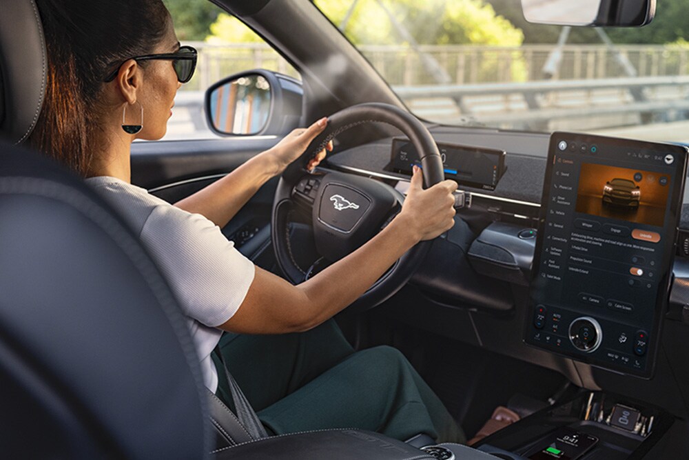 Une femme conduisant la Mustang Mach-E avec ses mains sur le volant. L’écran tactile de 15,5" indiquant des informations sur la voiture.