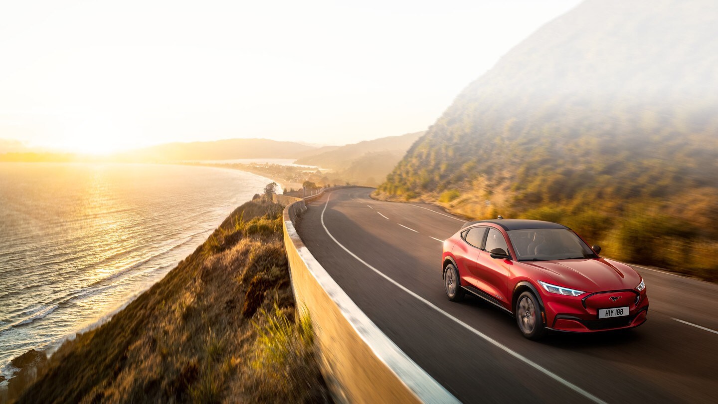 Red All-electric Mustang Mach-E driving past lake on mountain road