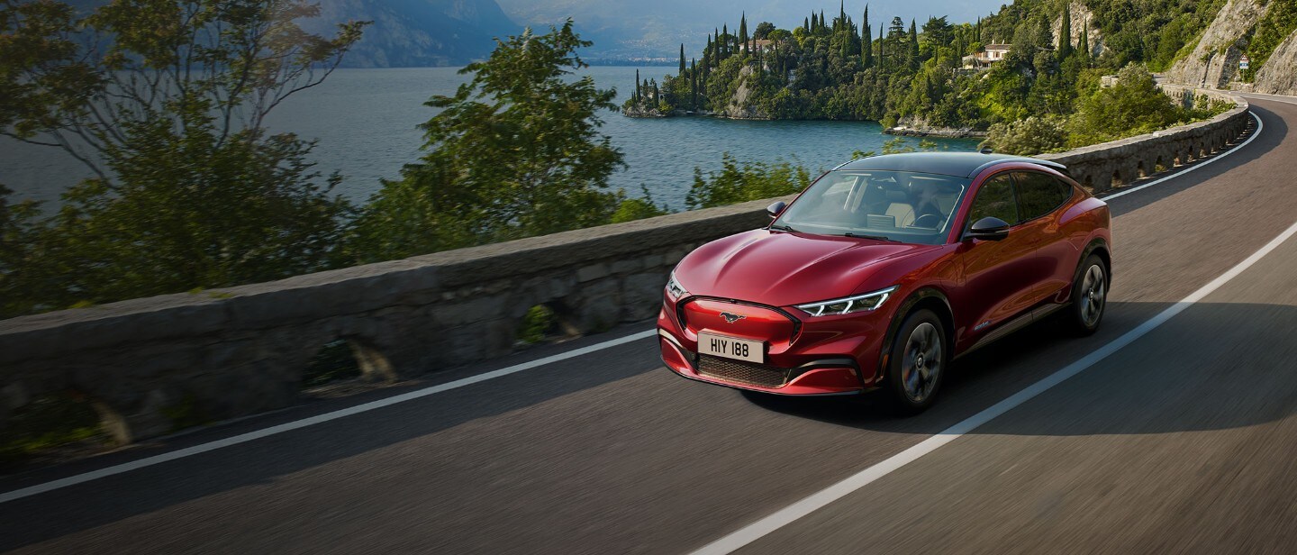 Red all-electric Ford Mach-E driving past the mountain lake