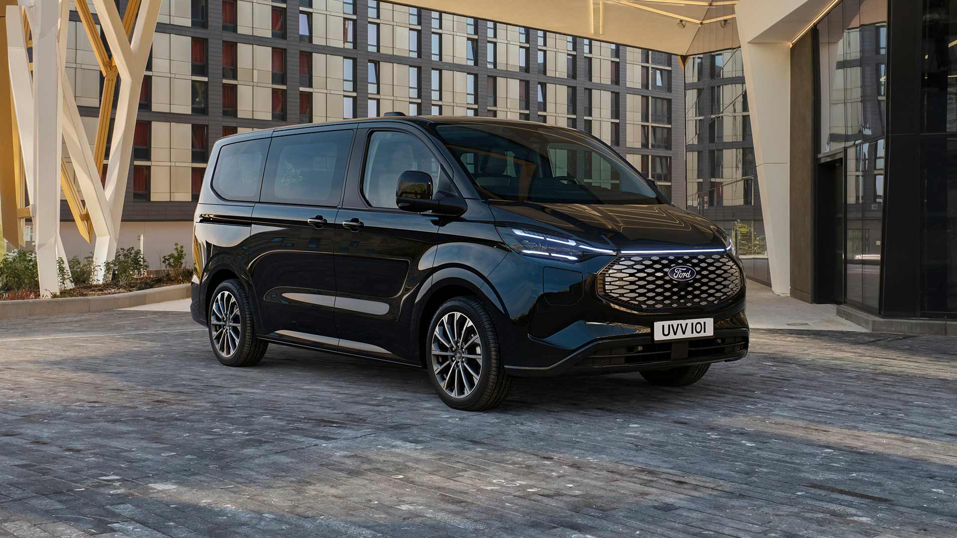 Un Ford E-Tourneo Custom noir est stationné devant un bâtiment moderne.