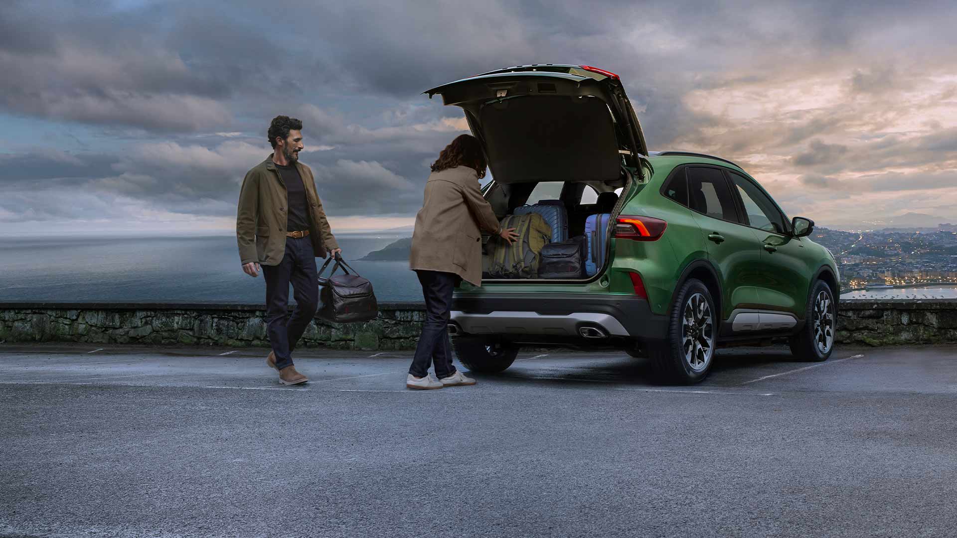 Deux personnes chargeant plusieurs valises dans le coffre spacieux du Ford Kuga. 