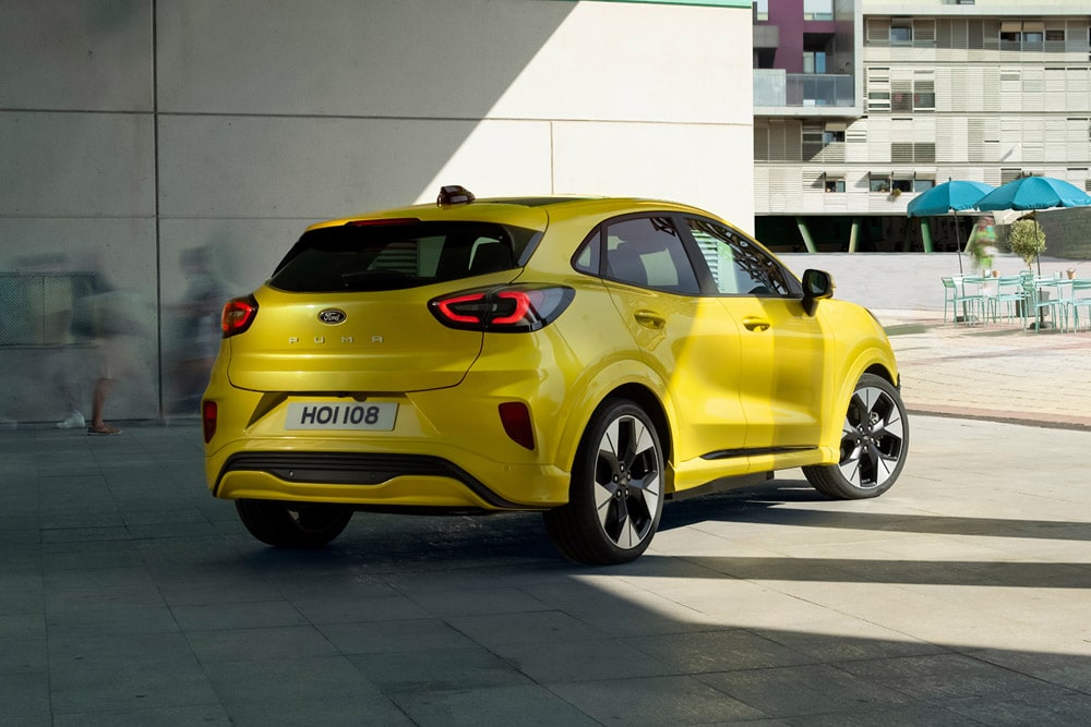 Vue de profil d'un Ford Puma Gen-E jaune stationné près d'un immeuble.