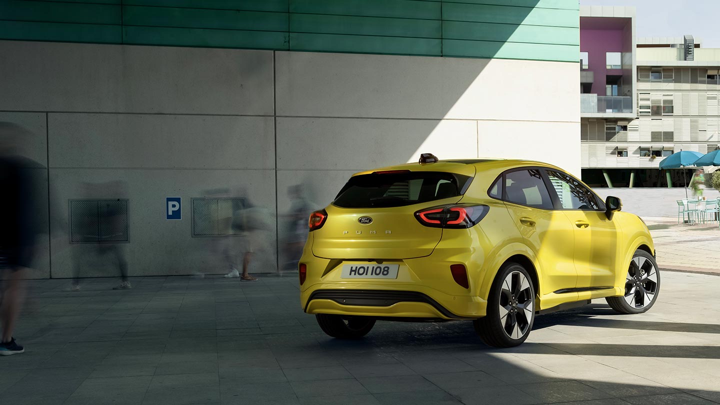 L’angle arrière d’un Ford Puma Gen-E® électrique jaune stationnée sous un pont.