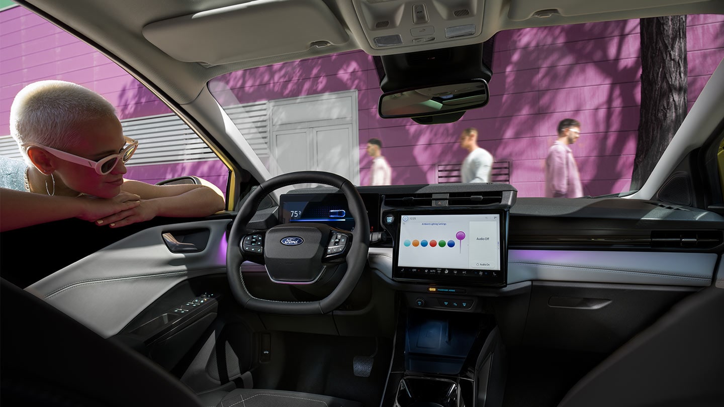 Personne regardant à l’intérieur du nouveau Ford Puma Gen-E®, montrant le grand écran tactile et l’éclairage ambiant.