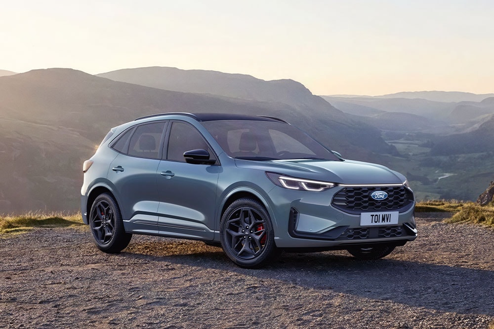 Un Ford Kuga gris garé sur une route de montagne en gravier au coucher du soleil.