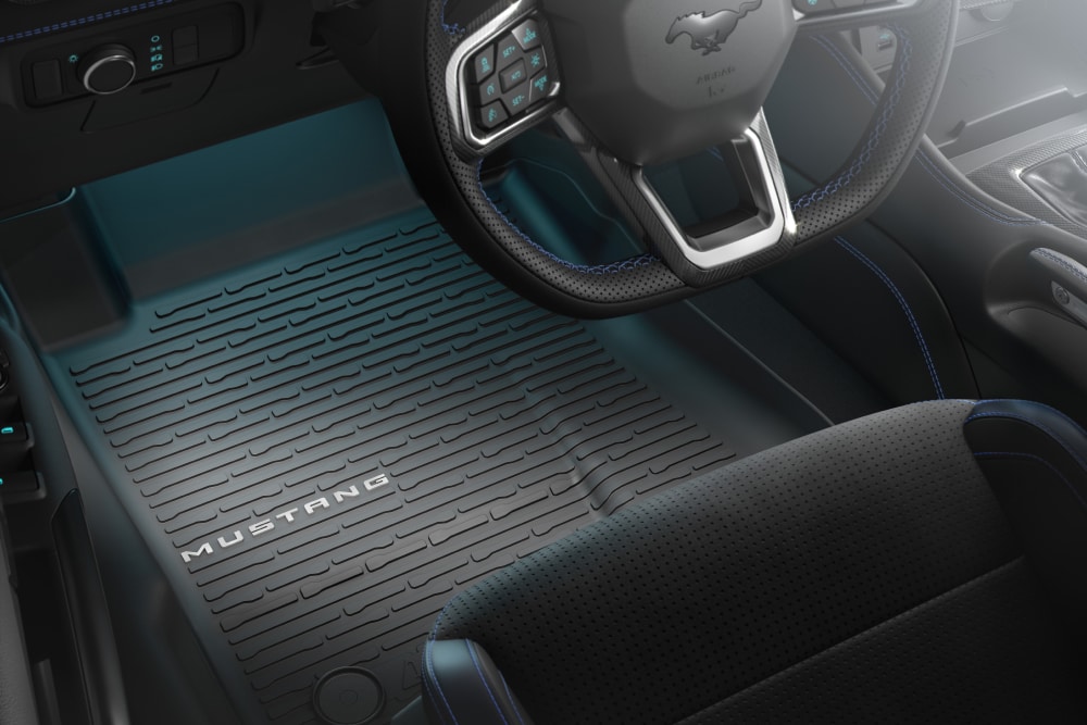 Vue de l'intérieur d'une Ford Mustang montrant le volant et un tapis de sol toutes saisons avec la marque « MUSTANG ».