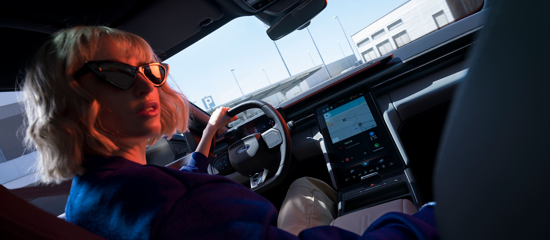 Une femme est assise sur le siège conducteur d’un Ford Capri® garée, avec vue sur le volant et le grand écran tactile SYNC® Move.
