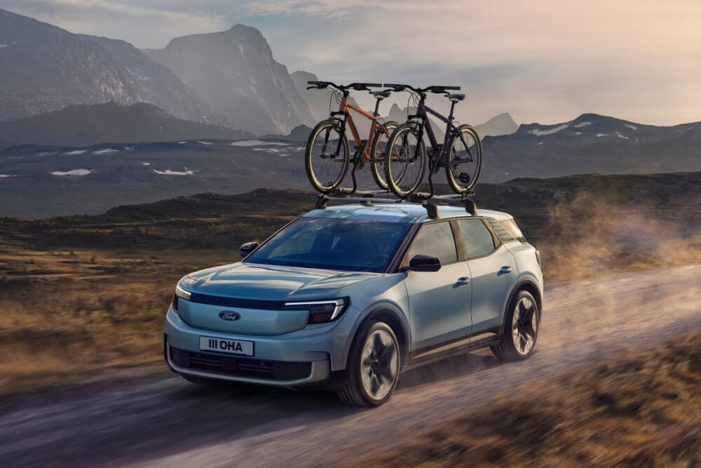 Ford Explorer de couleur bleue circulant sur un chemin de terre, avec barres de toit, porte-vélos et deux vélos montés sur le toit.