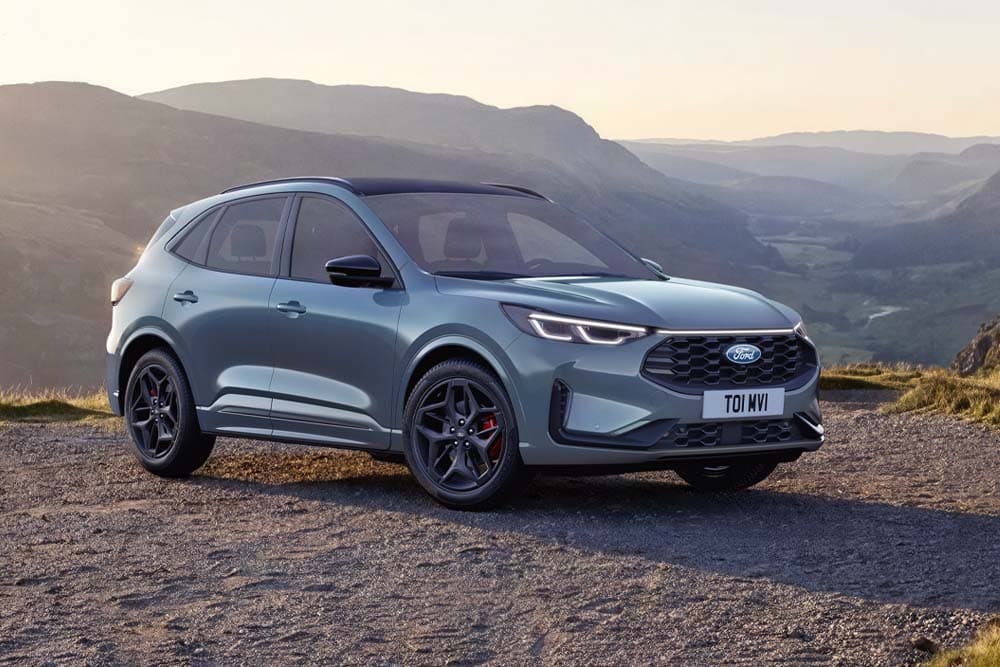 Un Ford Kuga gris garé sur une route de montagne en gravier au coucher du soleil.