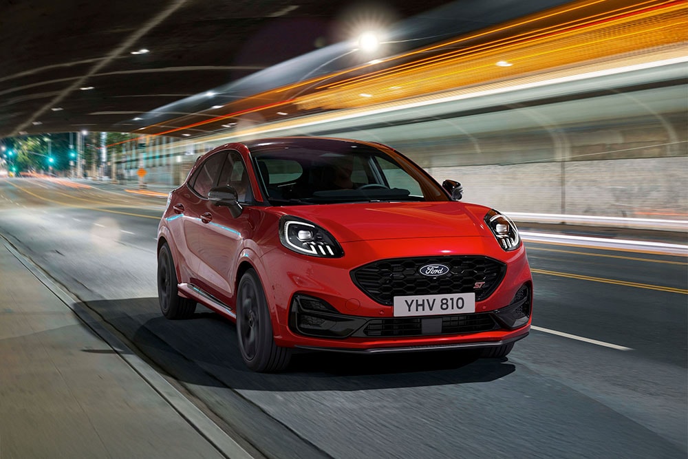 SUV sportif Ford Puma ST rouge circulant de nuit sur une route urbaine illuminée.