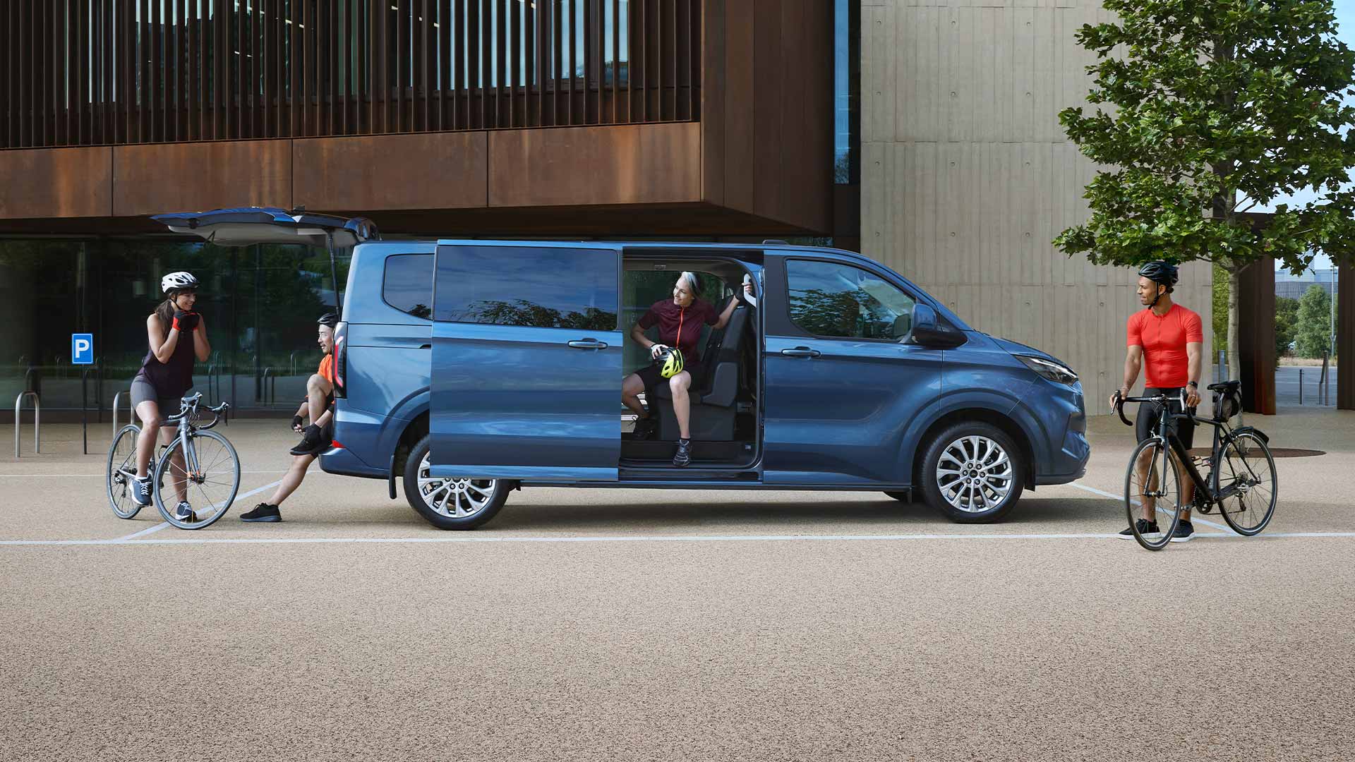 Ford Tourneo Custom bleu stationné avec les portes latérales ouvertes et des personnes avec des vélos à proximité. 