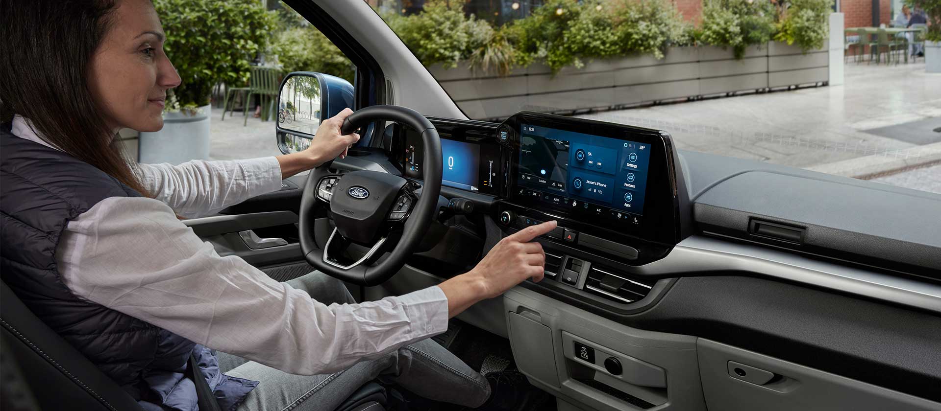 Une femme assise au volant du Ford E-Tourneo Custom, interagissant avec l’écran tactile central.