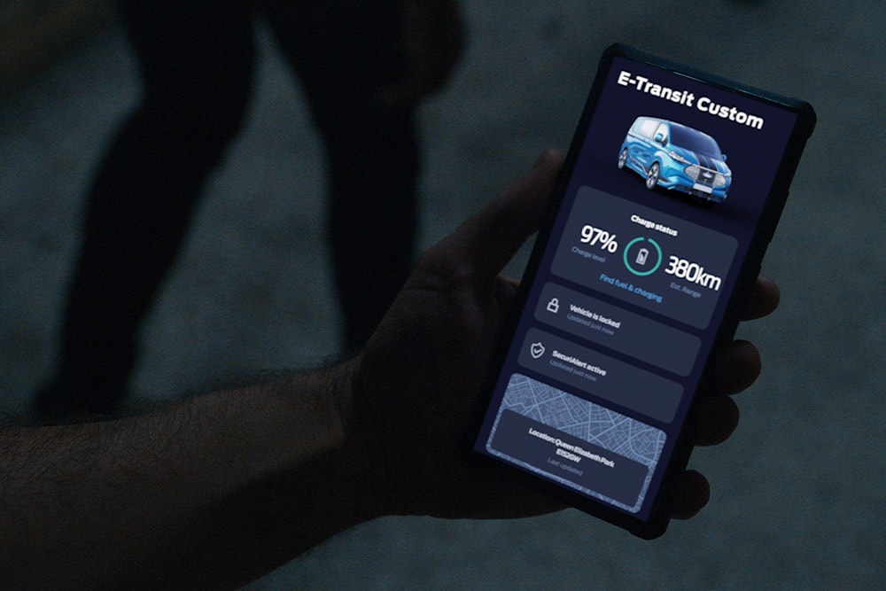 Un smartphone affichant un E-Transit Custom dans l’App FordPass, indiquant le niveau de charge du véhicule et son emplacement.