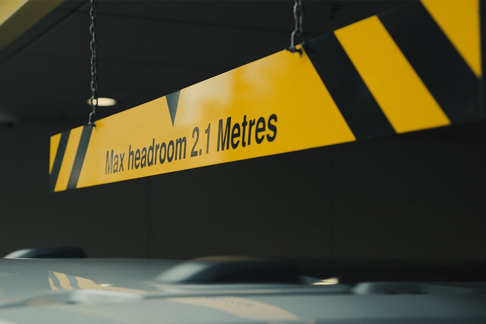 Panneau jaune et noir dans un parking couvert indiquant « Hauteur maximale 2,1 mètres ».