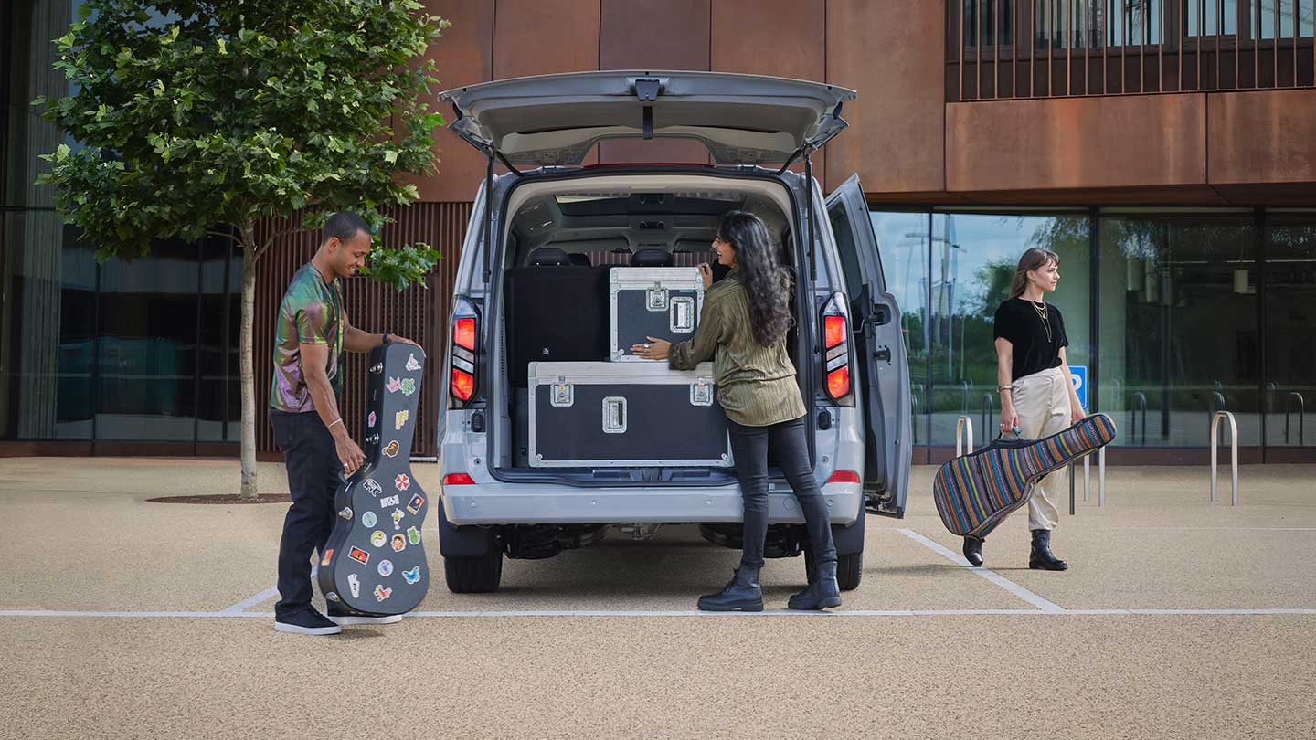 L’arrière d’un Ford Tourneo Custom couleur argent est ouvert, avec des personnes qui chargent un équipement musical à l’arrière.