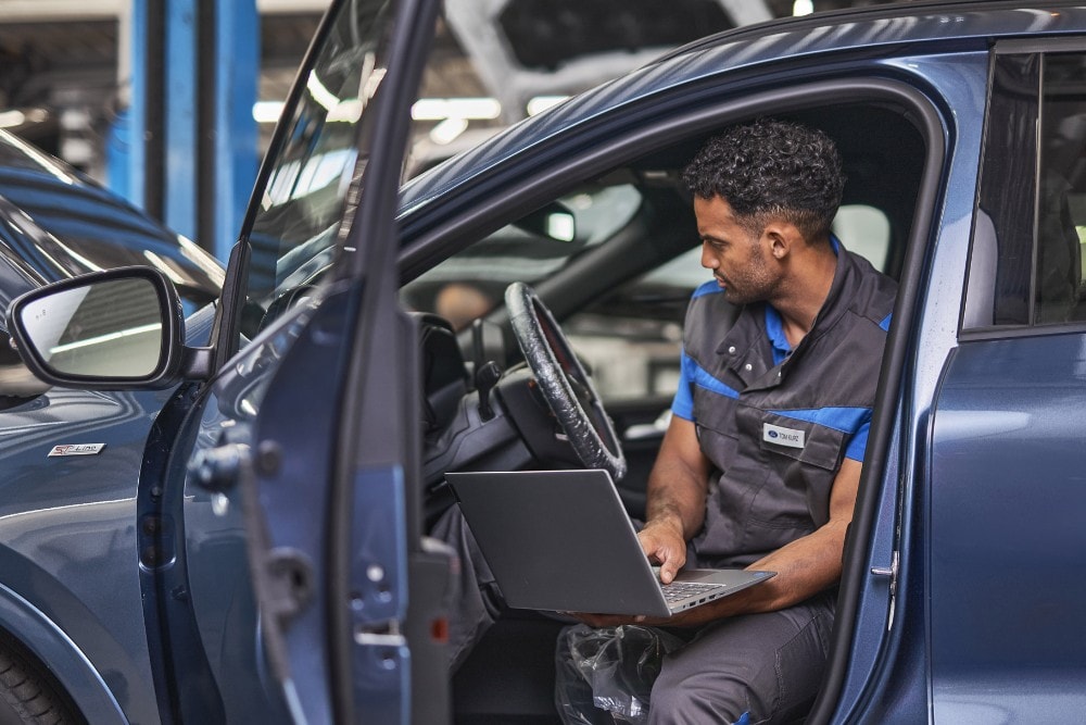 Technicien Ford utilisant un ordinateur portable lors de l’entretien d’un véhicule avec la porte conducteur ouverte.