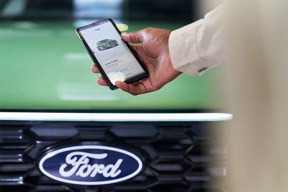  Personne tenant un smartphone affichant l’application FordPass devant la calandre d’un véhicule Ford.