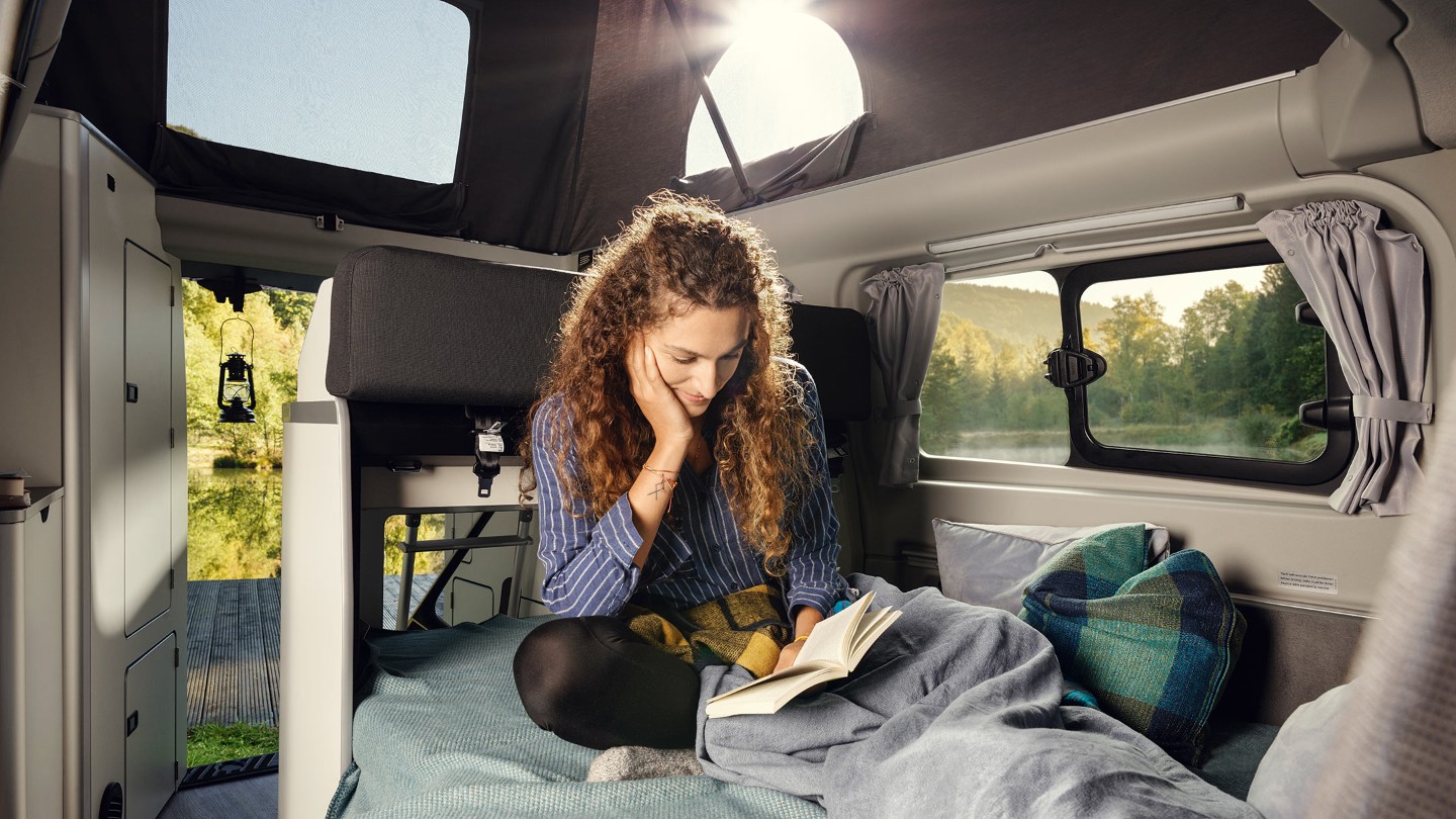 Woman siting and reading in Ford Transit Custom Nugget interior with lifted roof