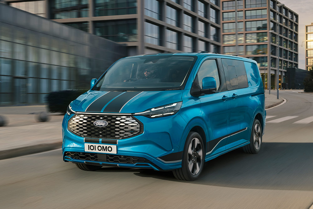Un fourgon Ford E-Transit Custom Sport Multi-use bleu roule dans la rue d'une ville.