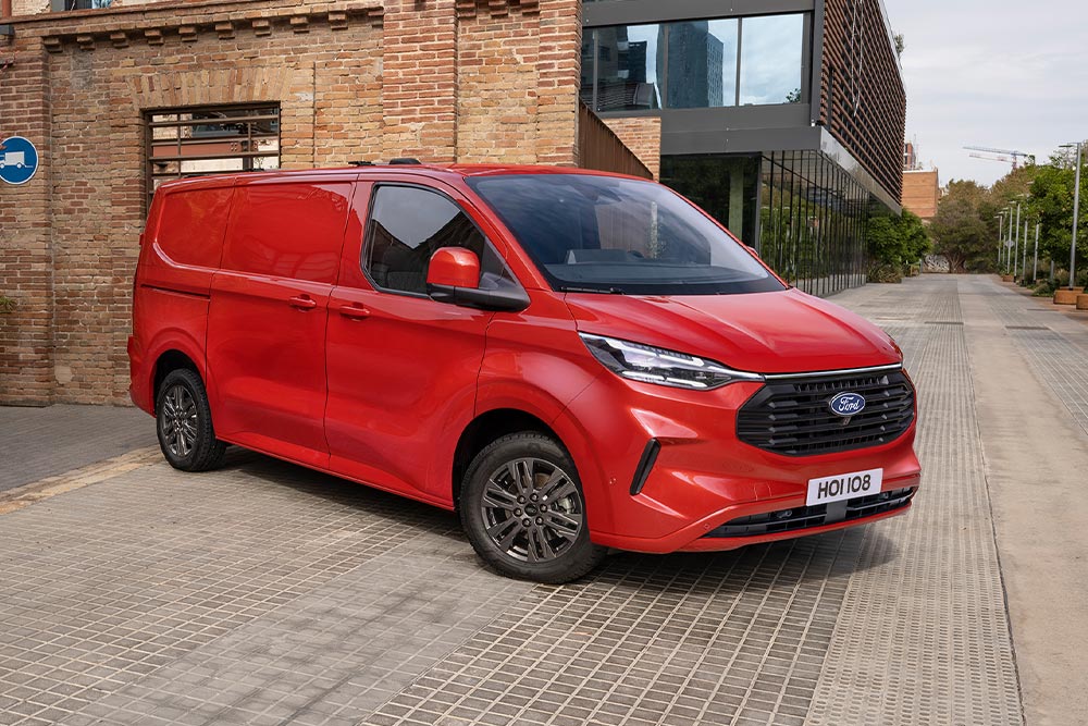 Fourgon Ford Transit Custom rouge stationné dans la rue d'une ville.