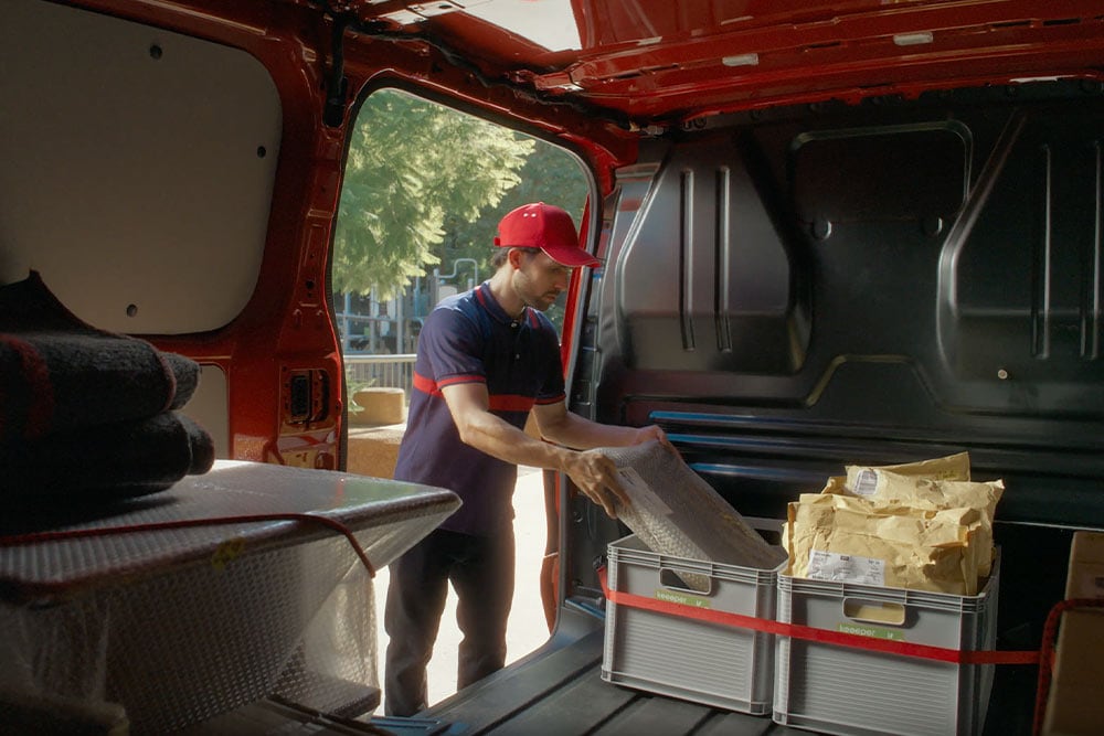 Un livreur décharge des colis d'un Ford Transit Custom rouge.