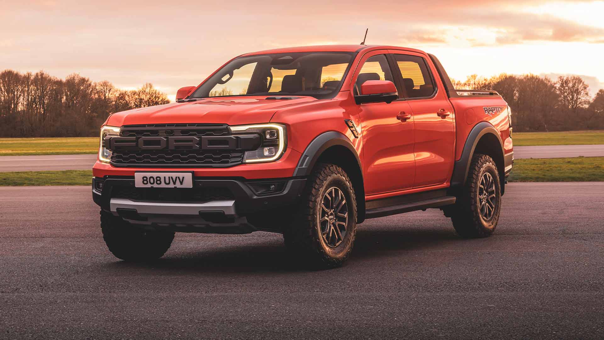 Ford Ranger Raptor en couleur Code Orange garé sur une piste, phares allumés. 